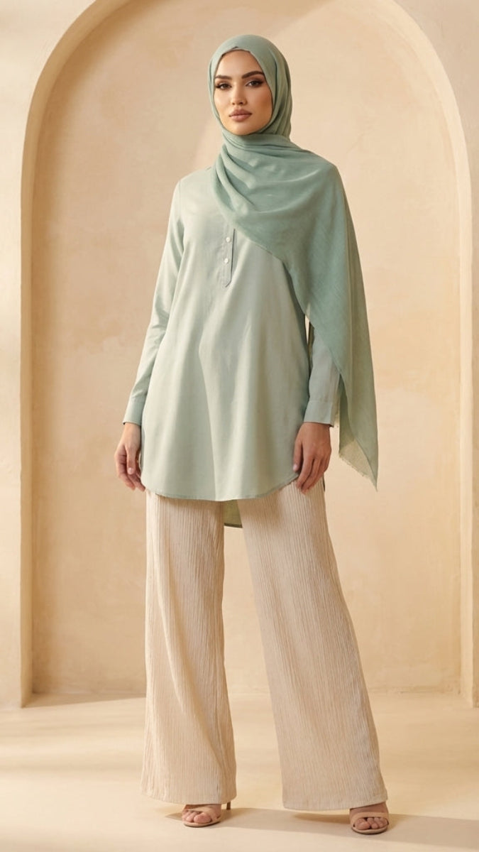 Woman wearing a light green hijab and beige outfit against a beige background