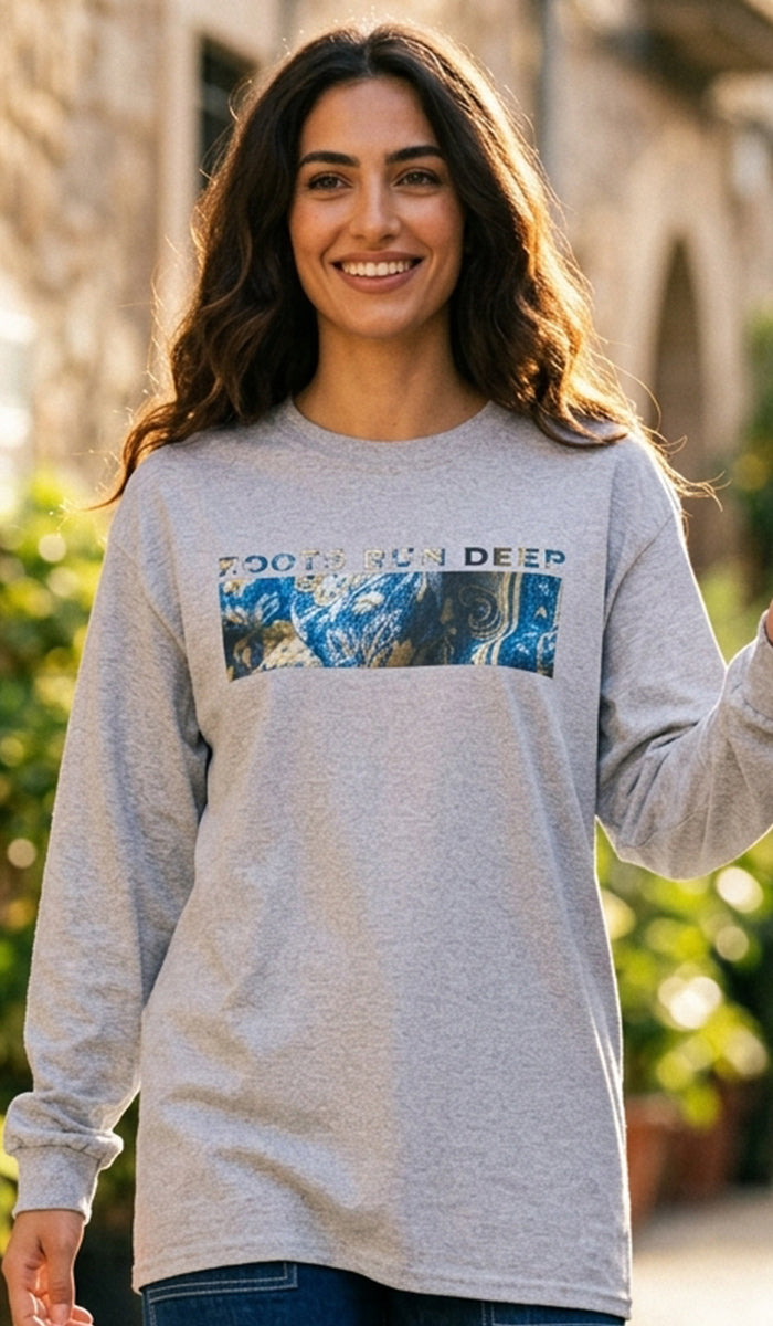 A woman smiling outdoors wearing a light heather gray long-sleeve t-shirt with a graphic print that reads 'TOO MUCH SUN DEEP' above a blue and white abstract design.
