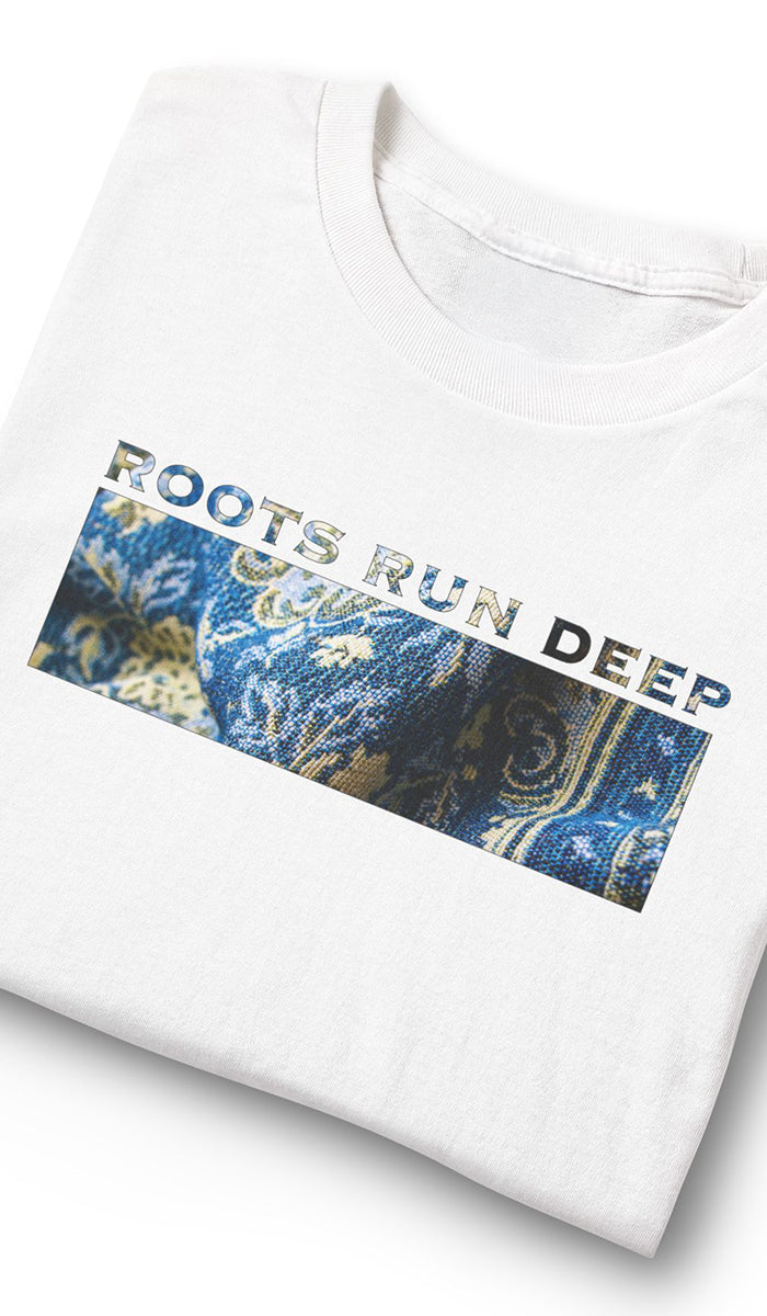 A folded white t-shirt with a graphic print on the front. The graphic features the text 'ROOTS RUN DEEP' in a distressed font over a rectangular blue and gold patterned design.