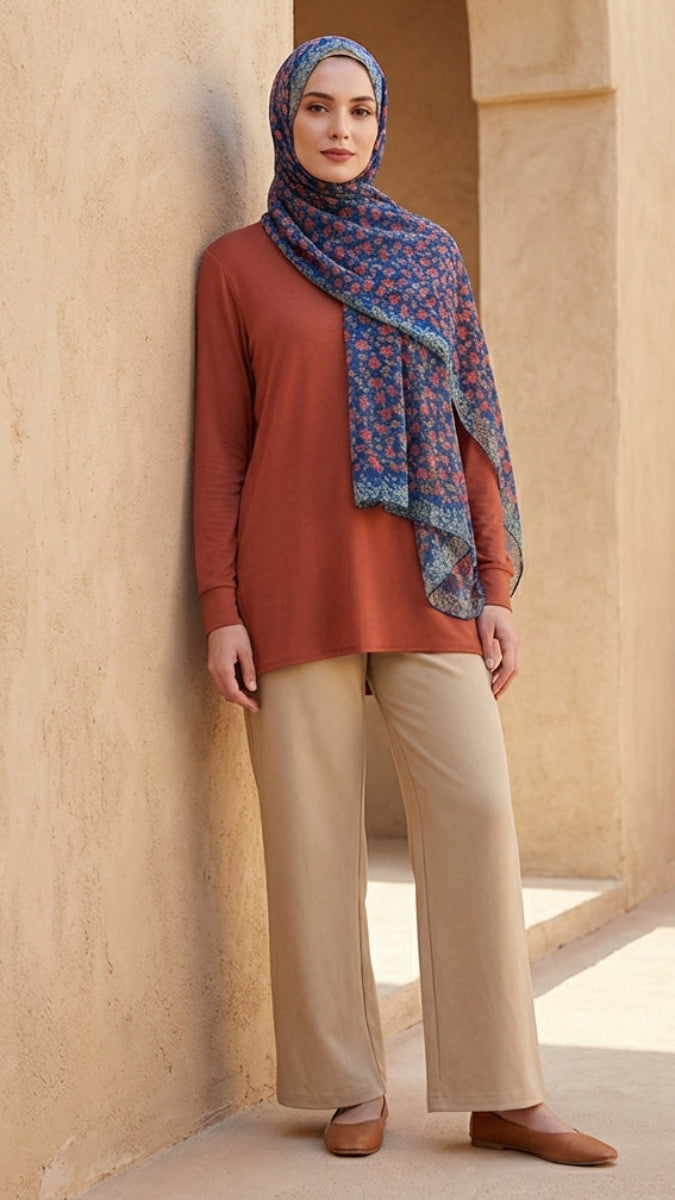 Woman wearing a rust-colored top and beige pants with a patterned scarf in a sunlit room.