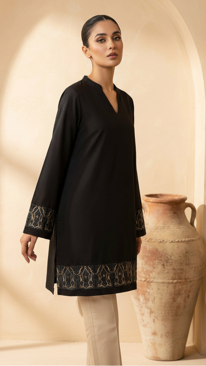 Woman wearing a black embroidered dress standing in a warm-toned interior setting with clay pots.