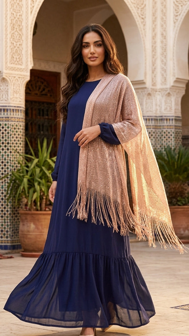 Woman in a blue dress with a beige shawl standing in a decorative outdoor setting.