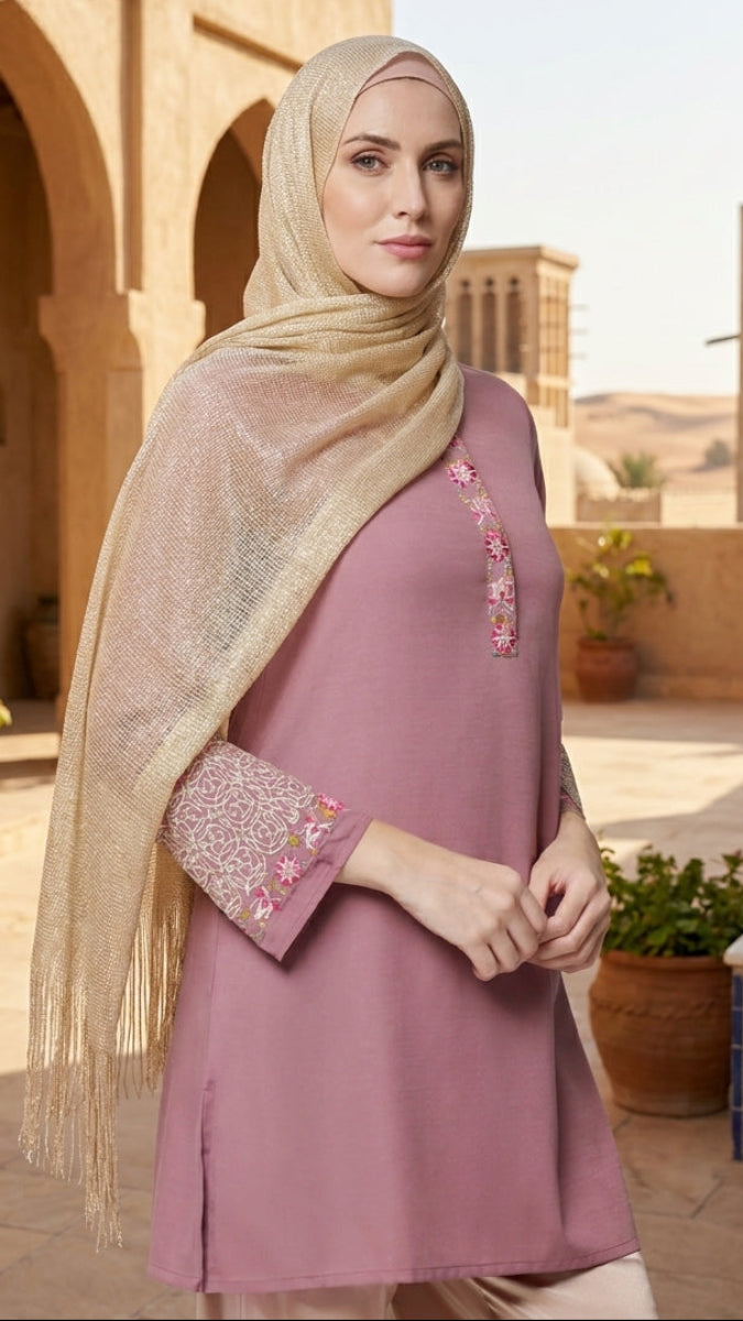 Woman in a pink dress with floral embroidery standing in a desert courtyard.