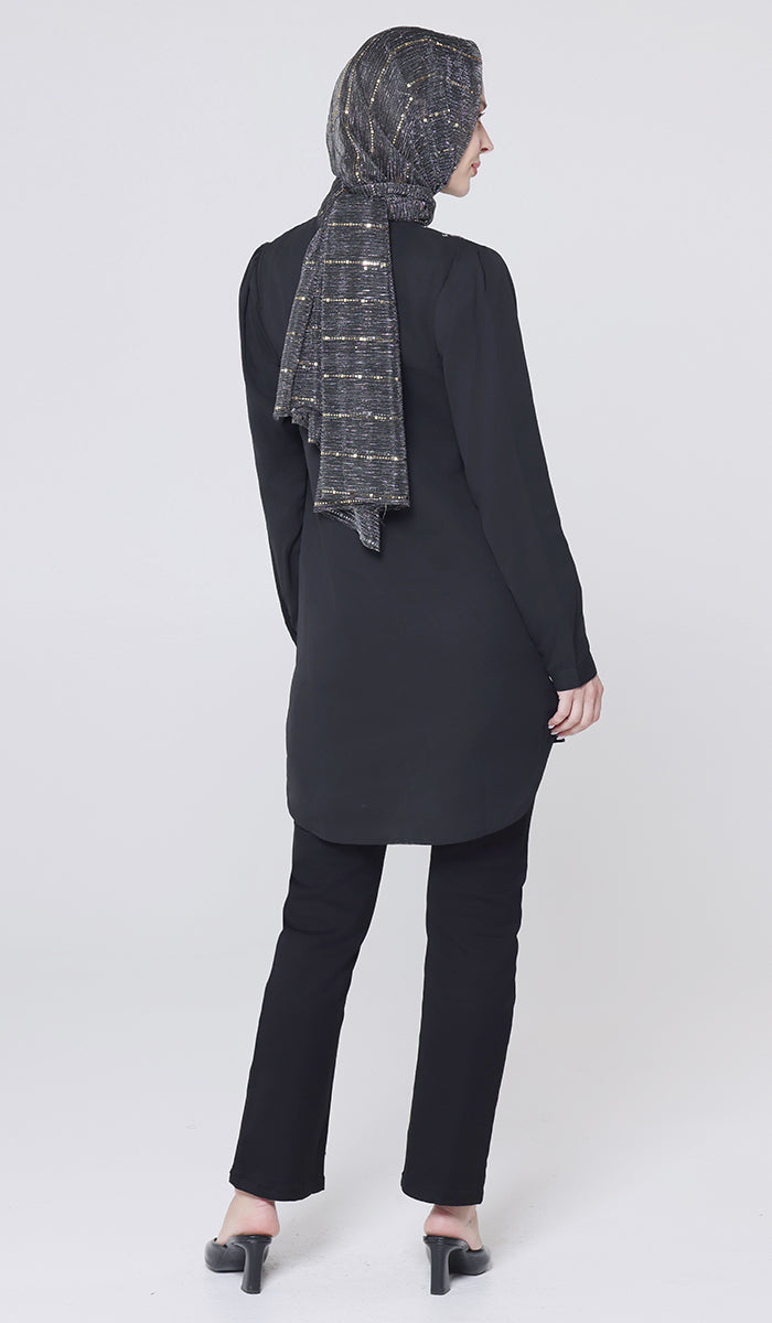 Person wearing a black outfit with a patterned scarf on a white background