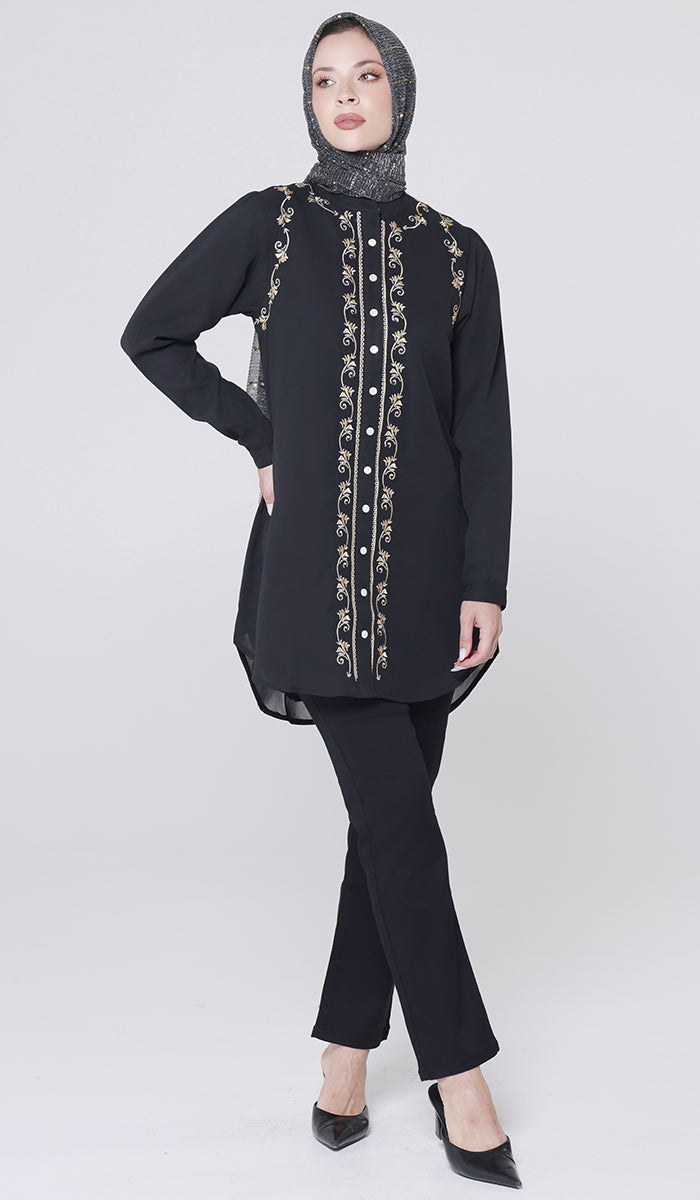 Woman wearing a black embroidered top and pants with a hijab on a white background