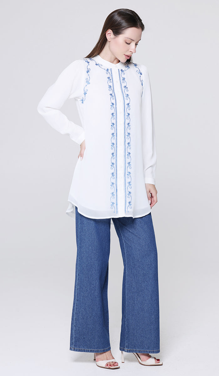 Woman wearing a white embroidered top and blue jeans on a white background