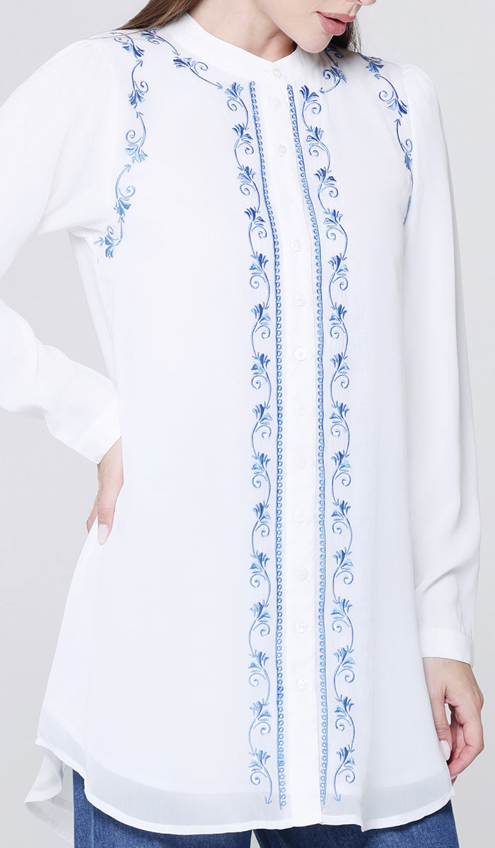 White blouse with blue embroidery on a plain background