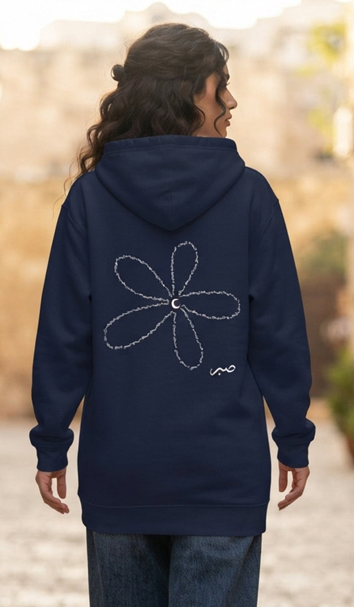 A woman viewed from behind wearing a navy blue hoodie with a white flower graphic on the back, standing outdoors against a blurred background.