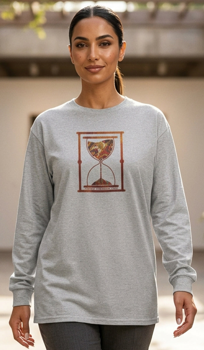A woman wearing a light gray long-sleeve t-shirt with a graphic of an hourglass containing a map of the world, set against a blurred outdoor background.