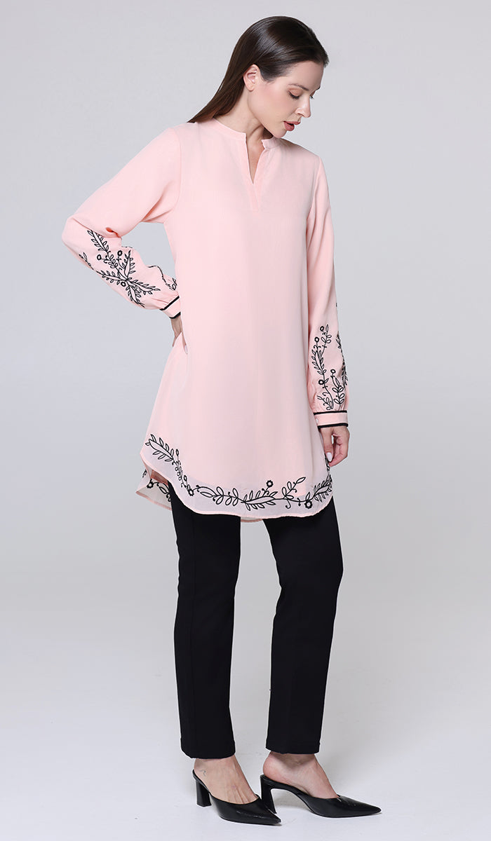 Woman wearing a pink blouse with black embroidery and black pants on a white background