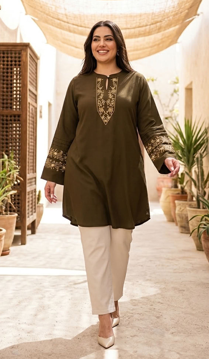 A woman models a dark olive green kurta with gold embroidery on the neckline and cuffs, paired with beige trousers, walking in a sunlit courtyard with plants and a hanging canopy.