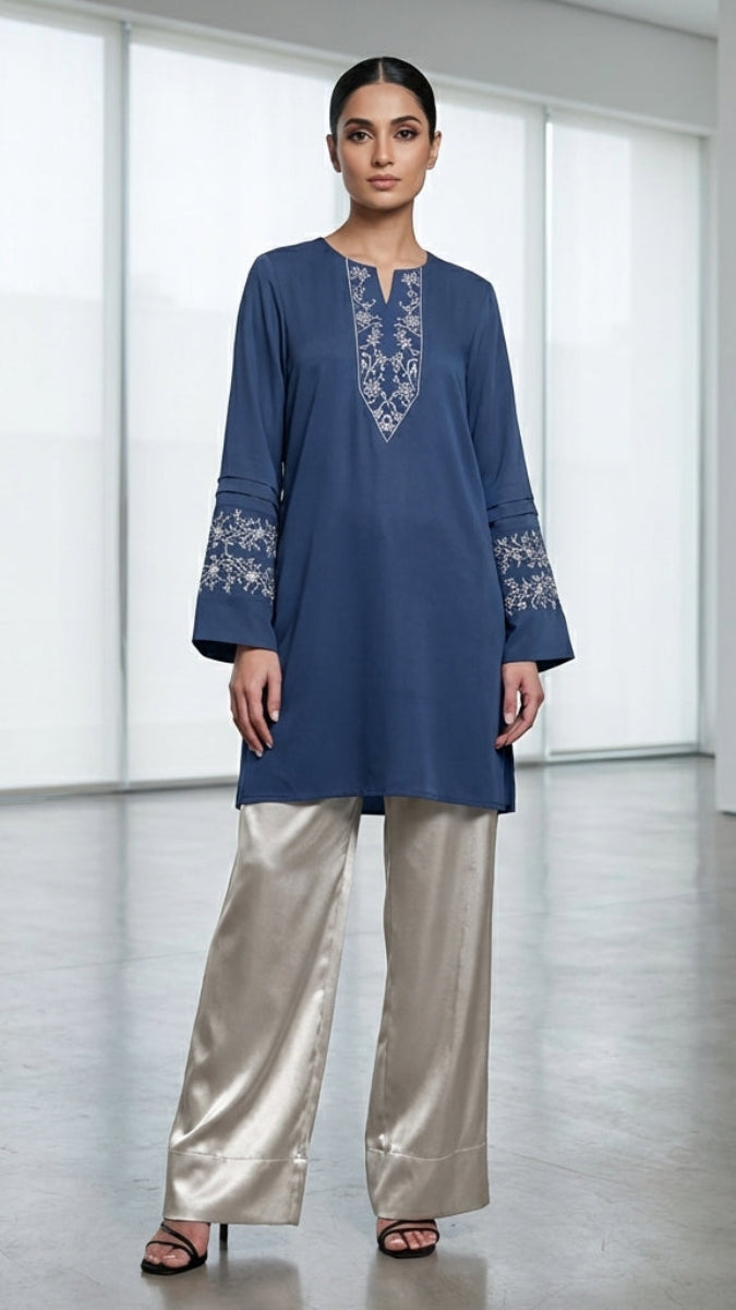 Woman wearing a blue embroidered top and silver pants in an art gallery setting