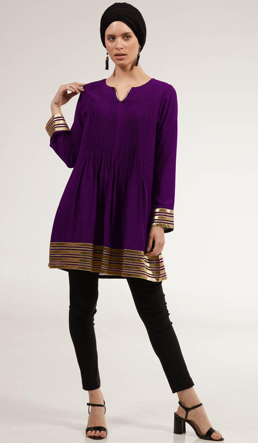 Woman with hand on her shoulder wearing Sultana tunic in Deep Plum with black pants and heels. 