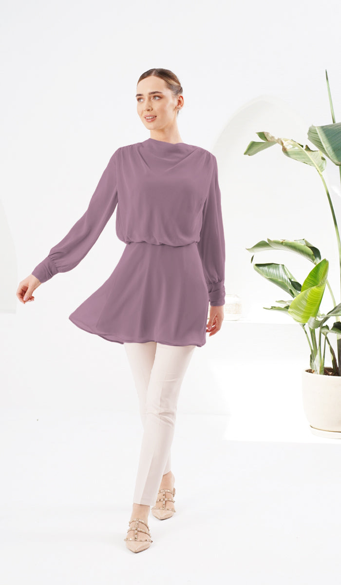 Woman smiling and wearing Myra chiffon tunic in Dusty Mauve, next to a plant.